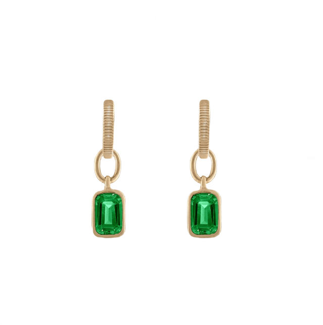 Emerald-hued gemstone earrings resting on a cream surface.